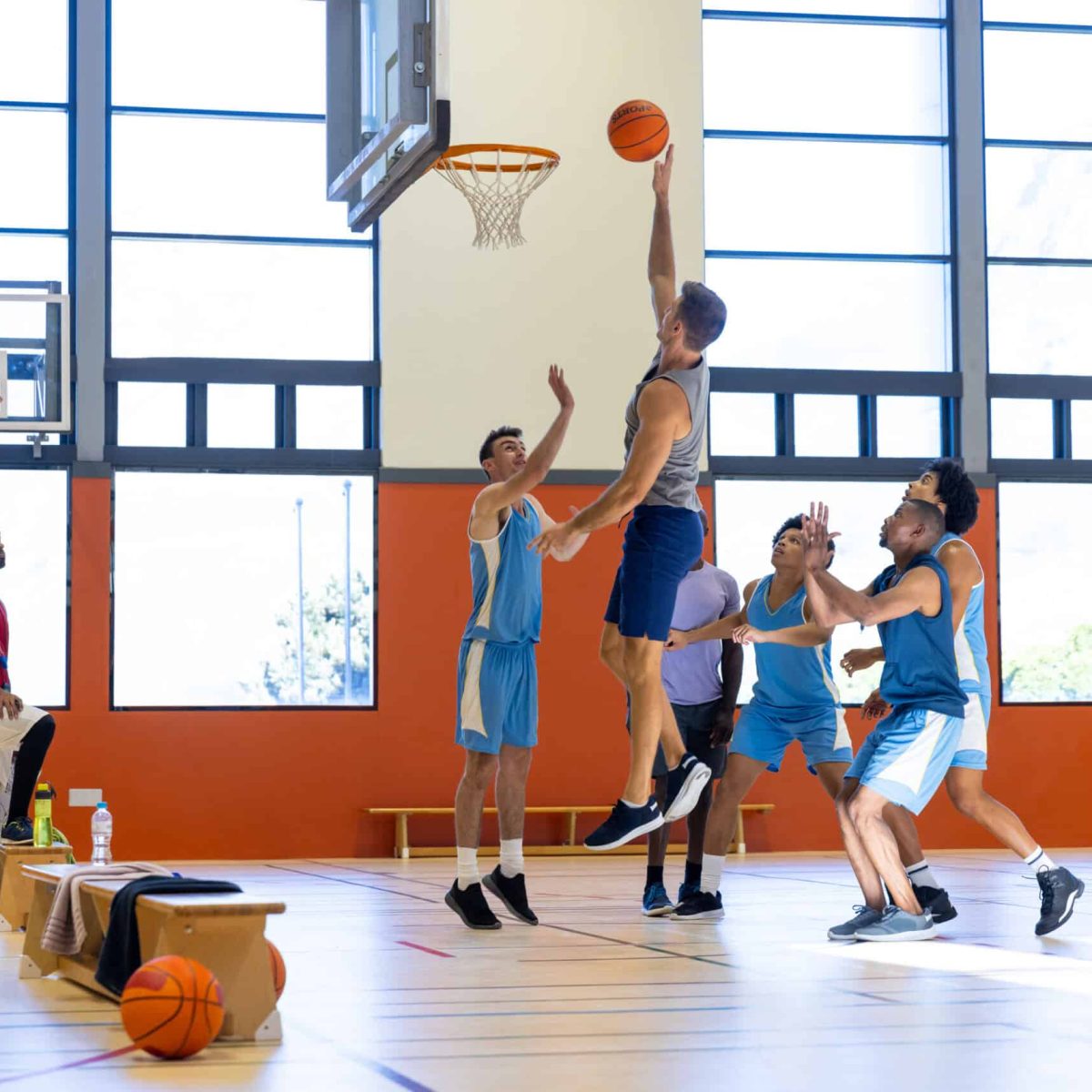 Diverse male basketball players wearing blue sports clothes and playing basketball with coach at gym. Sport, activity, teamwork and lifestyle, unaltered.
